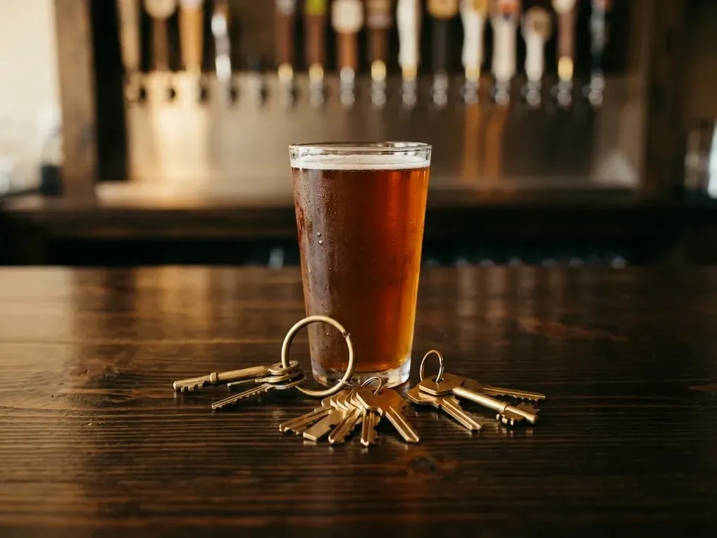 Brass keys and a pint of ale on a wood bar top in a Vista taproom